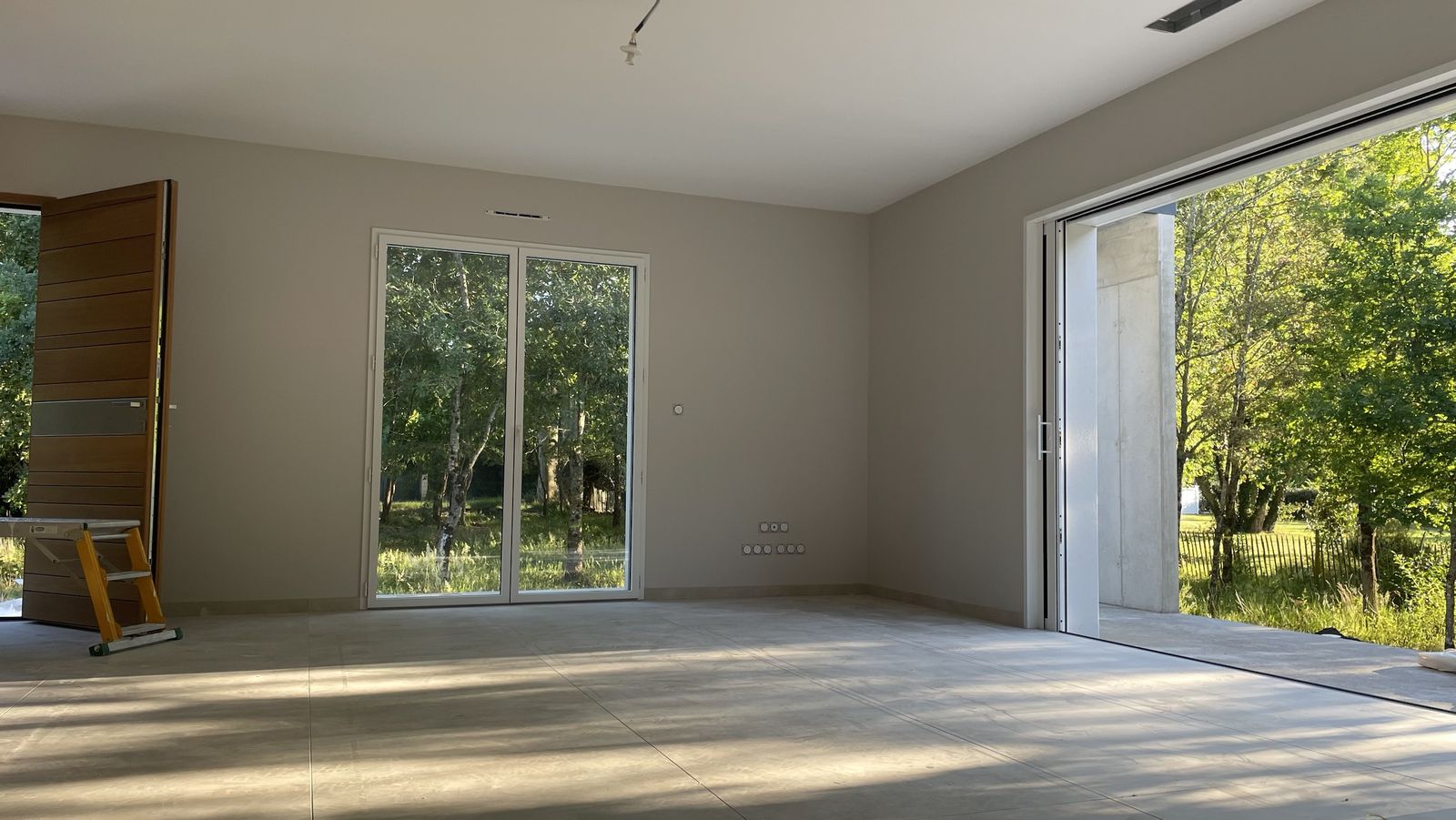 Pièce de vie d’une maison neuve : murs et plafonds peints, grandes baies vitrées ouvertes sur le jardin